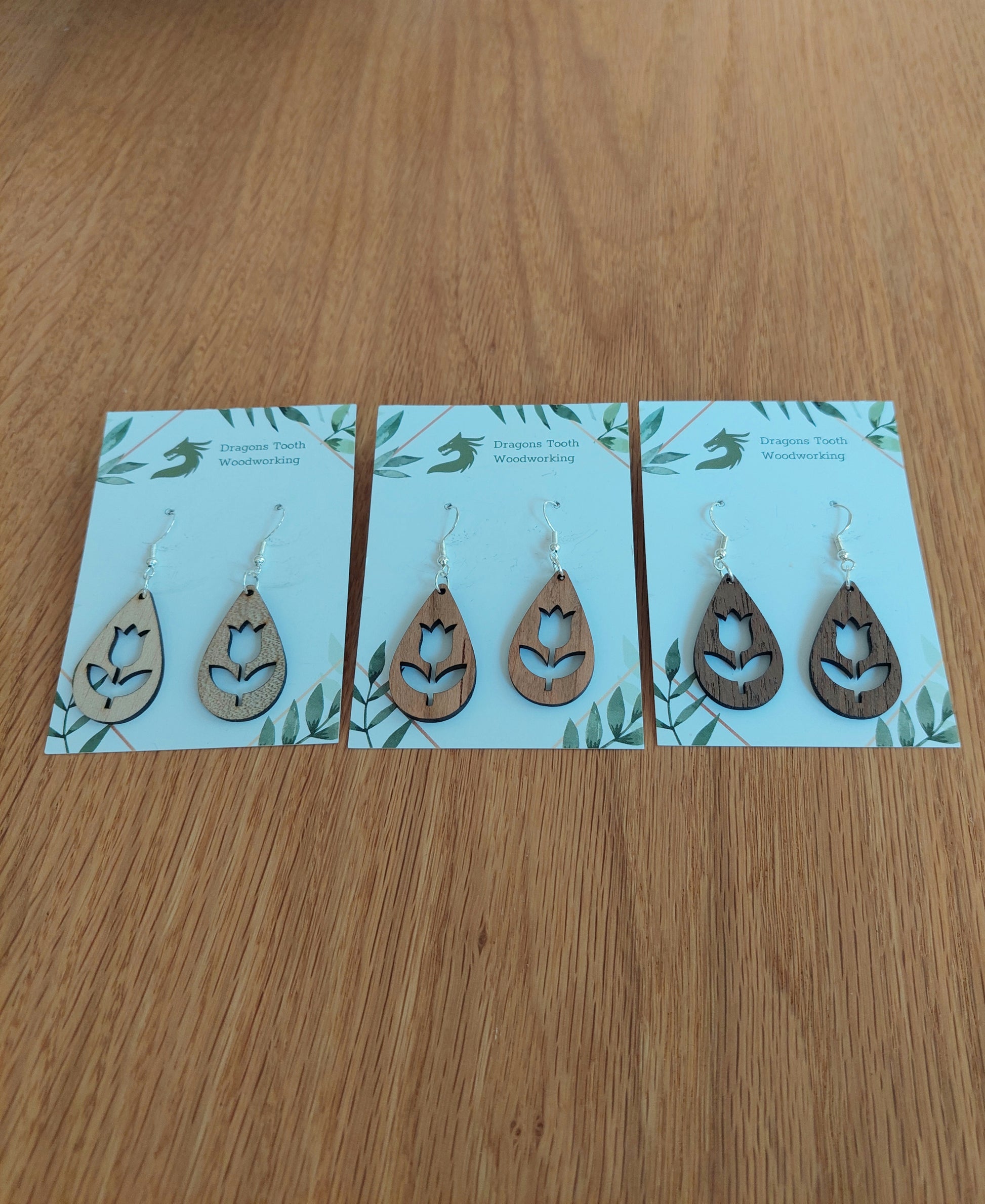 A beautiful collection of handcrafted wooden tulip flower dangle earrings displayed together in natural cherry, maple, and walnut hardwood finishes.