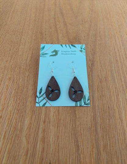 A pair of teardrop shaped earrings made from natural walnut hardwood, displayed on a card. The earring is laser-cut with a holly cluster design.