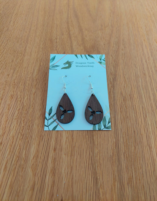 A pair of teardrop shaped earrings made from natural walnut hardwood, displayed on a card. The earring is laser-cut with a holly cluster design.