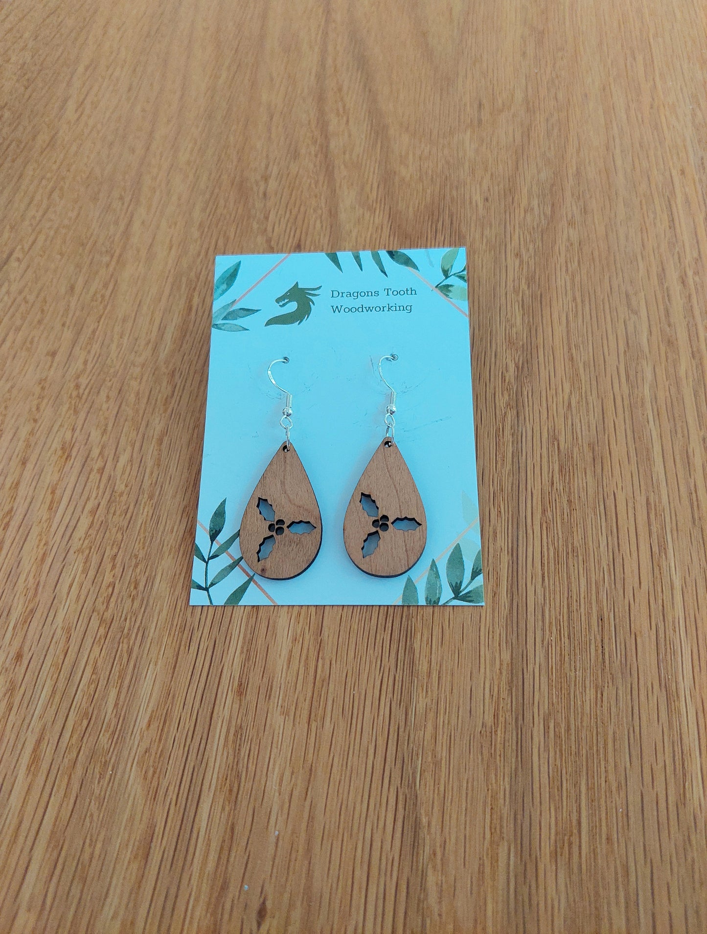 Front view of a pair of cherry wood holly cluster teardrop dangle earrings on an earring display card