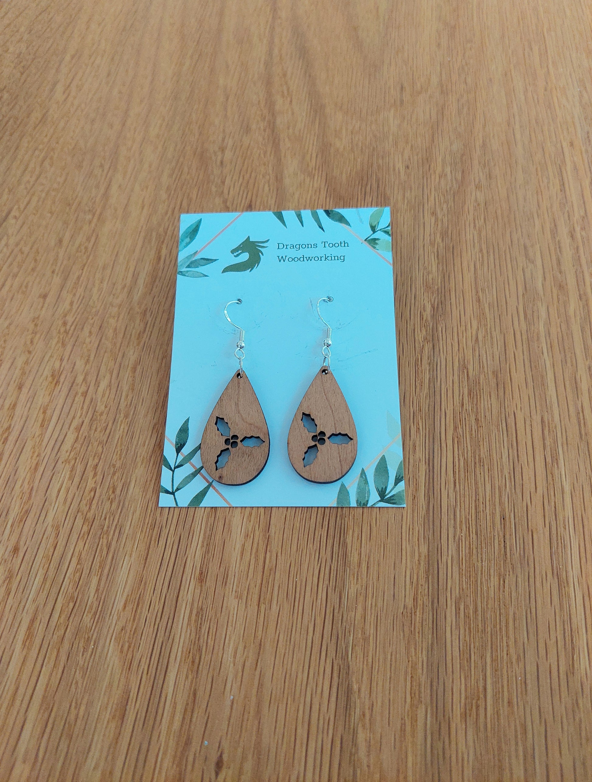 Front view of a pair of cherry wood holly cluster teardrop dangle earrings on an earring display card