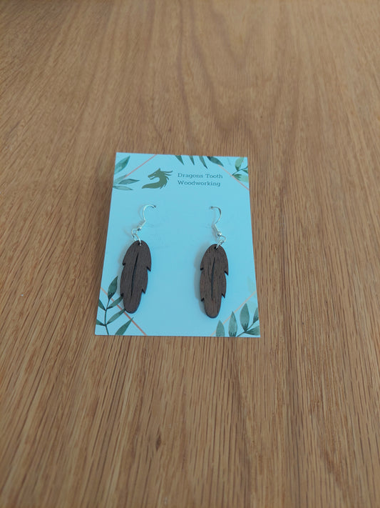 Front view of a pair of cherry wood intricate feather silhouette dangle earrings displayed on a rustic earring card.