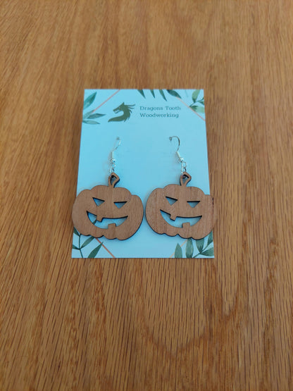 Front view of a pair of cherry wood jack-o'-lantern pumpkin dangle earrings displayed on a rustic earring card.