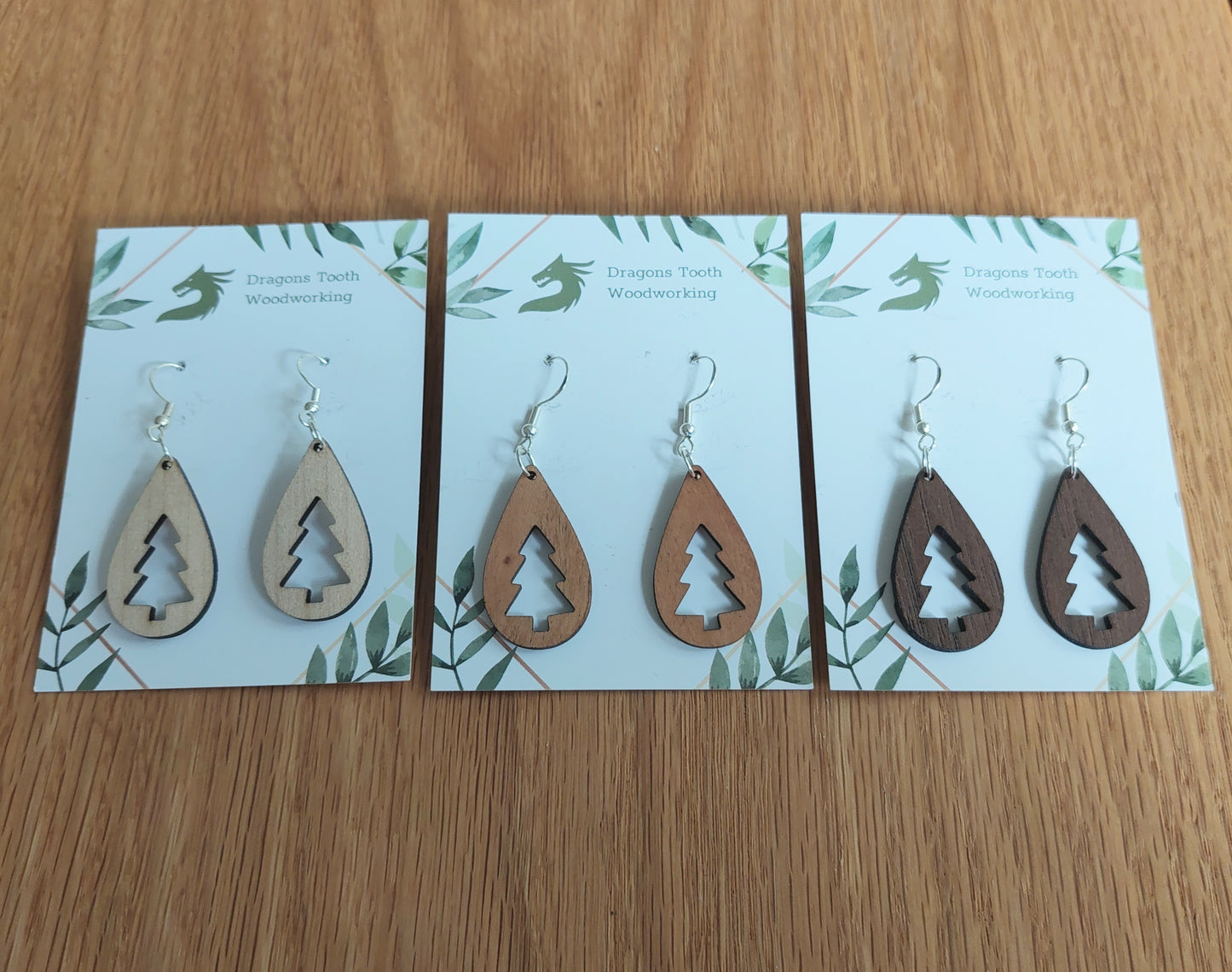 An alternate view displaying the Christmas tree teardrop earrings in three available wood types: light Maple, warm Cherry, and deep Walnut.