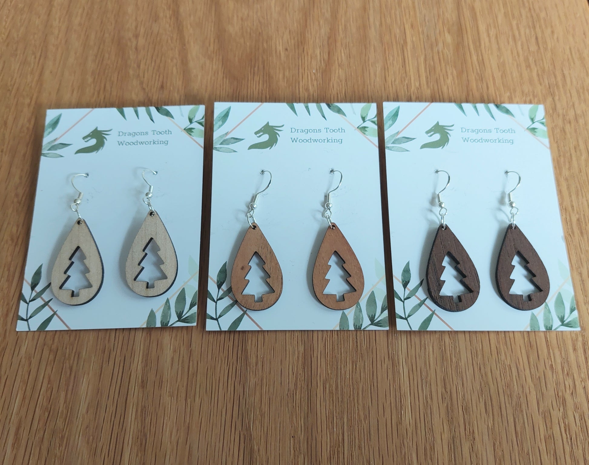 An alternate view displaying the Christmas tree teardrop earrings in three available wood types: light Maple, warm Cherry, and deep Walnut.