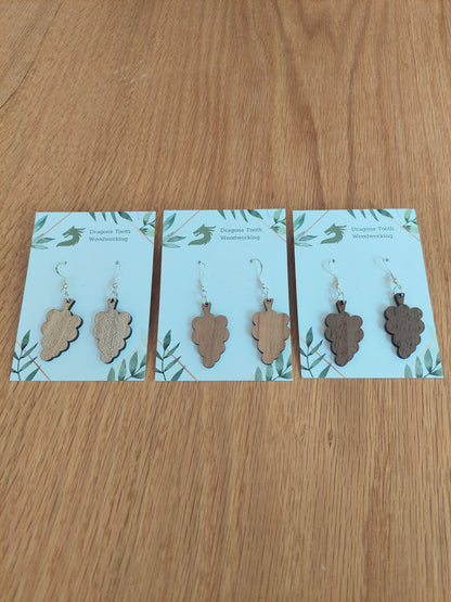 An alternate view displaying the grape cluster earrings in three available wood types: light Maple, warm Cherry, and deep Walnut.