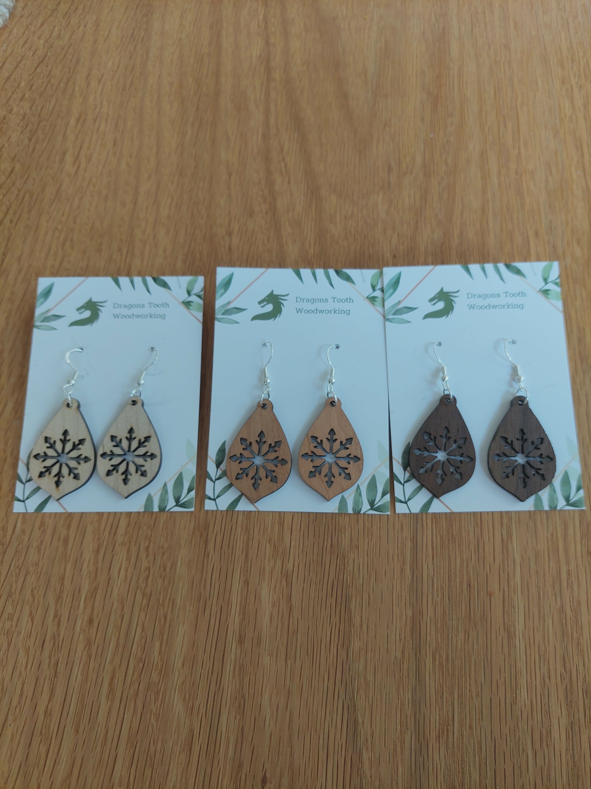 An alternate view displaying the large snowflake teardrop earrings in three available wood types: light Maple, warm Cherry, and deep Walnut.