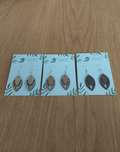 An alternate view displaying the monstera leaf earrings in three available wood types: light Maple, warm Cherry, and deep Walnut.