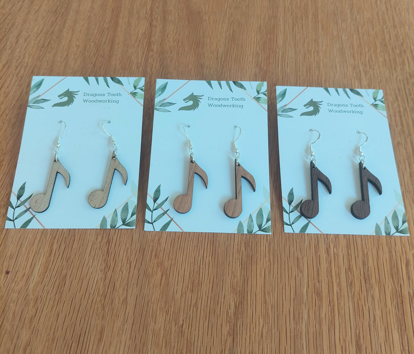 An alternate view displaying the circular music note earrings in three available wood types: light Maple, warm Cherry, and deep Walnut.