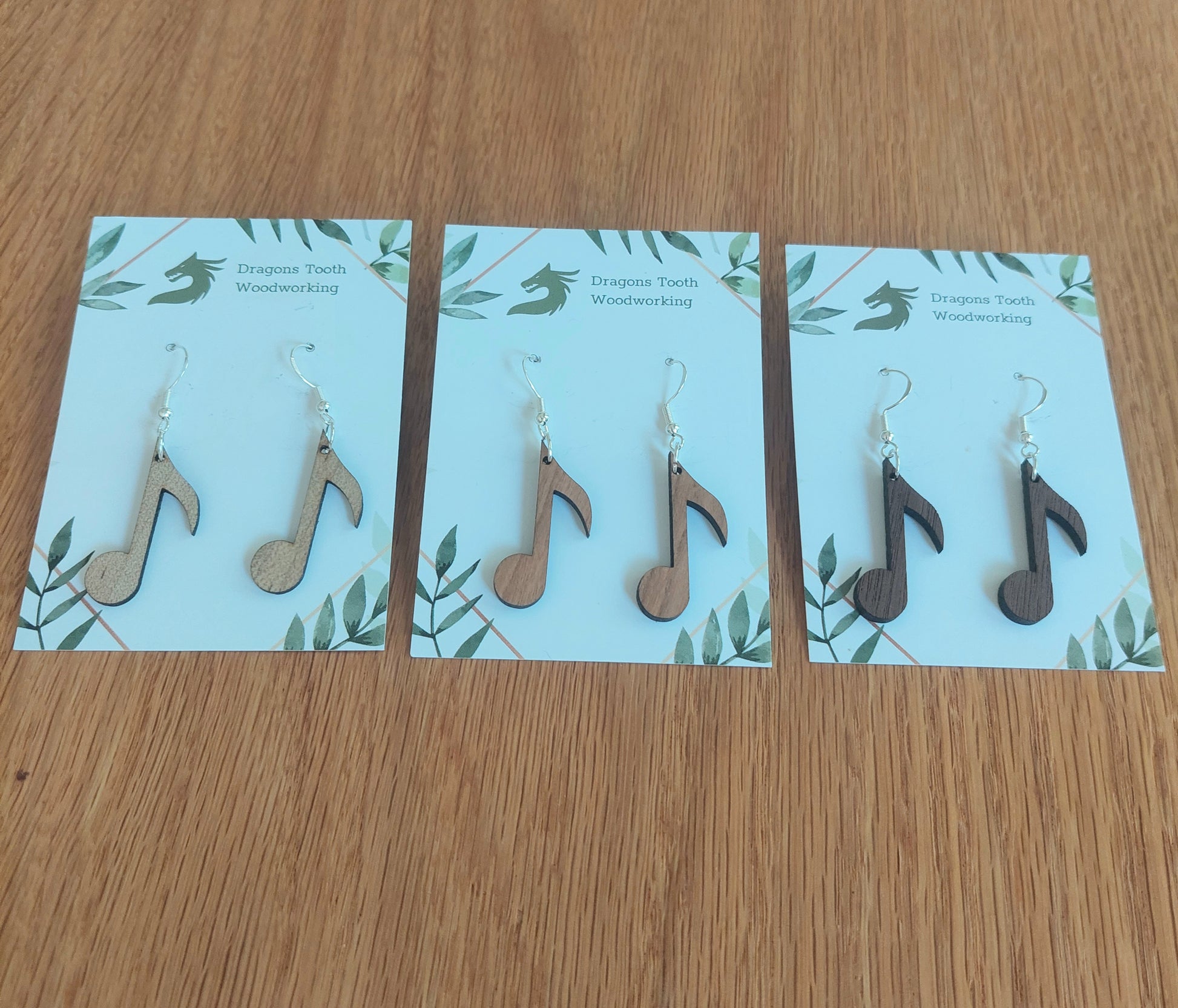 An alternate view displaying the circular music note earrings in three available wood types: light Maple, warm Cherry, and deep Walnut.
