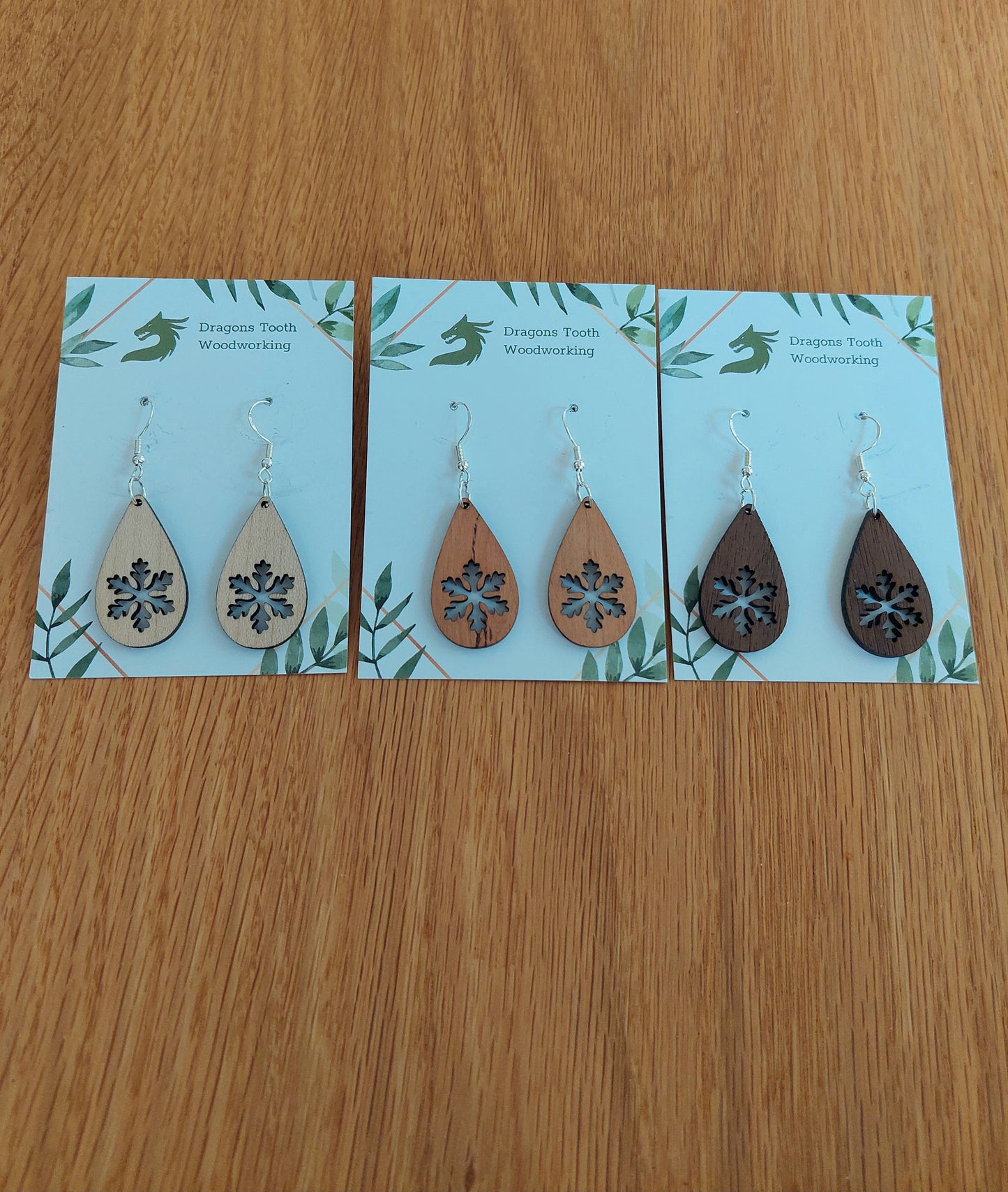 An alternate view displaying the snowflake teardrop earrings in three available wood types: light Maple, warm Cherry, and deep Walnut.