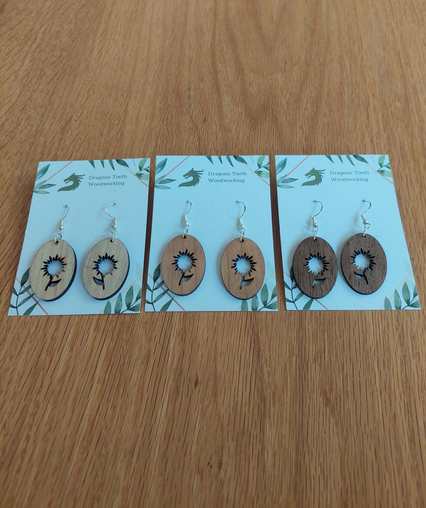 An alternate view displaying the aster flower silhouette dangle earrings in three available wood types: light Maple, warm Cherry, and deep Walnut.