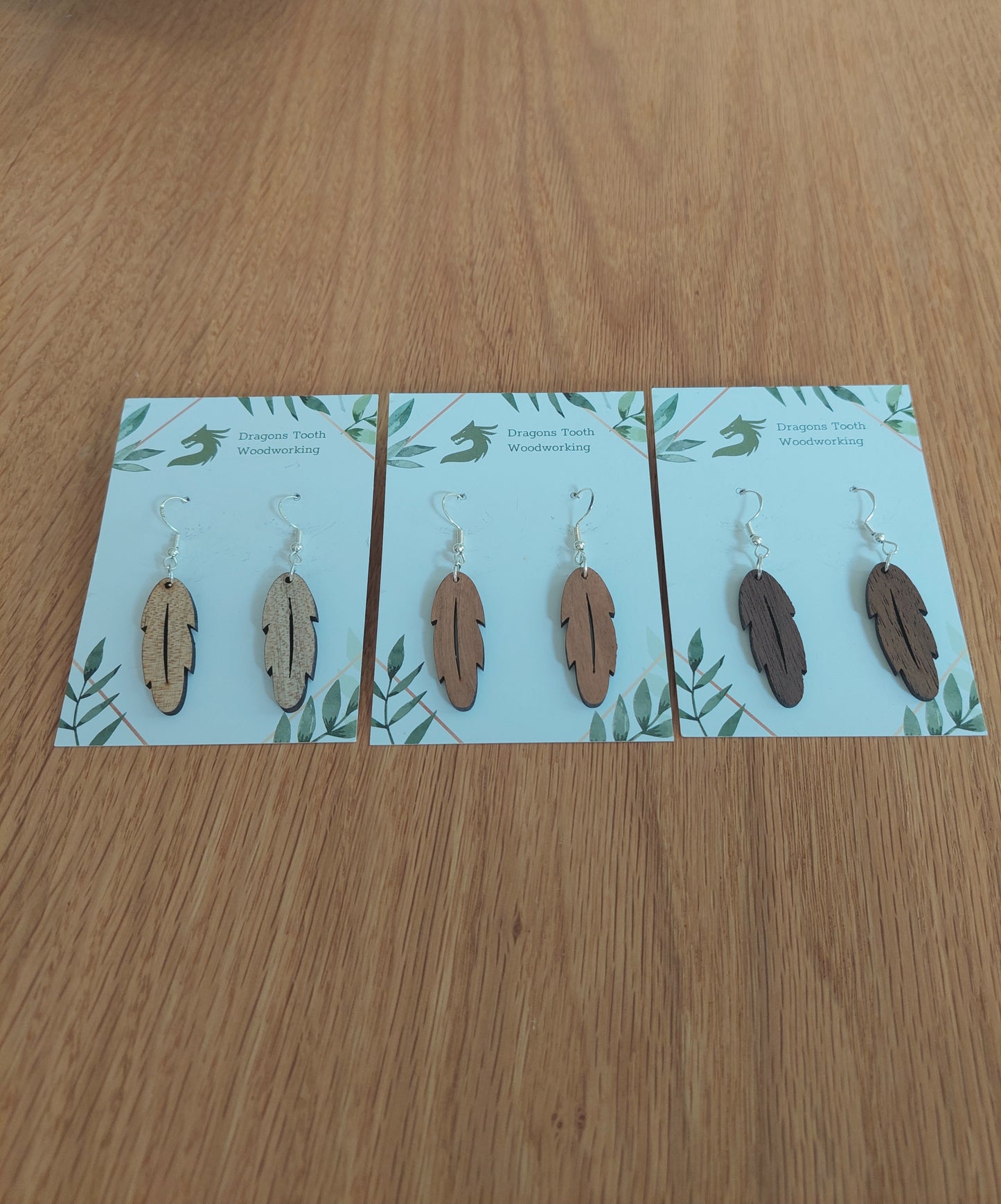 An alternate view displaying the bohemian feather earrings in three available wood types: light Maple, warm Cherry, and deep Walnut.