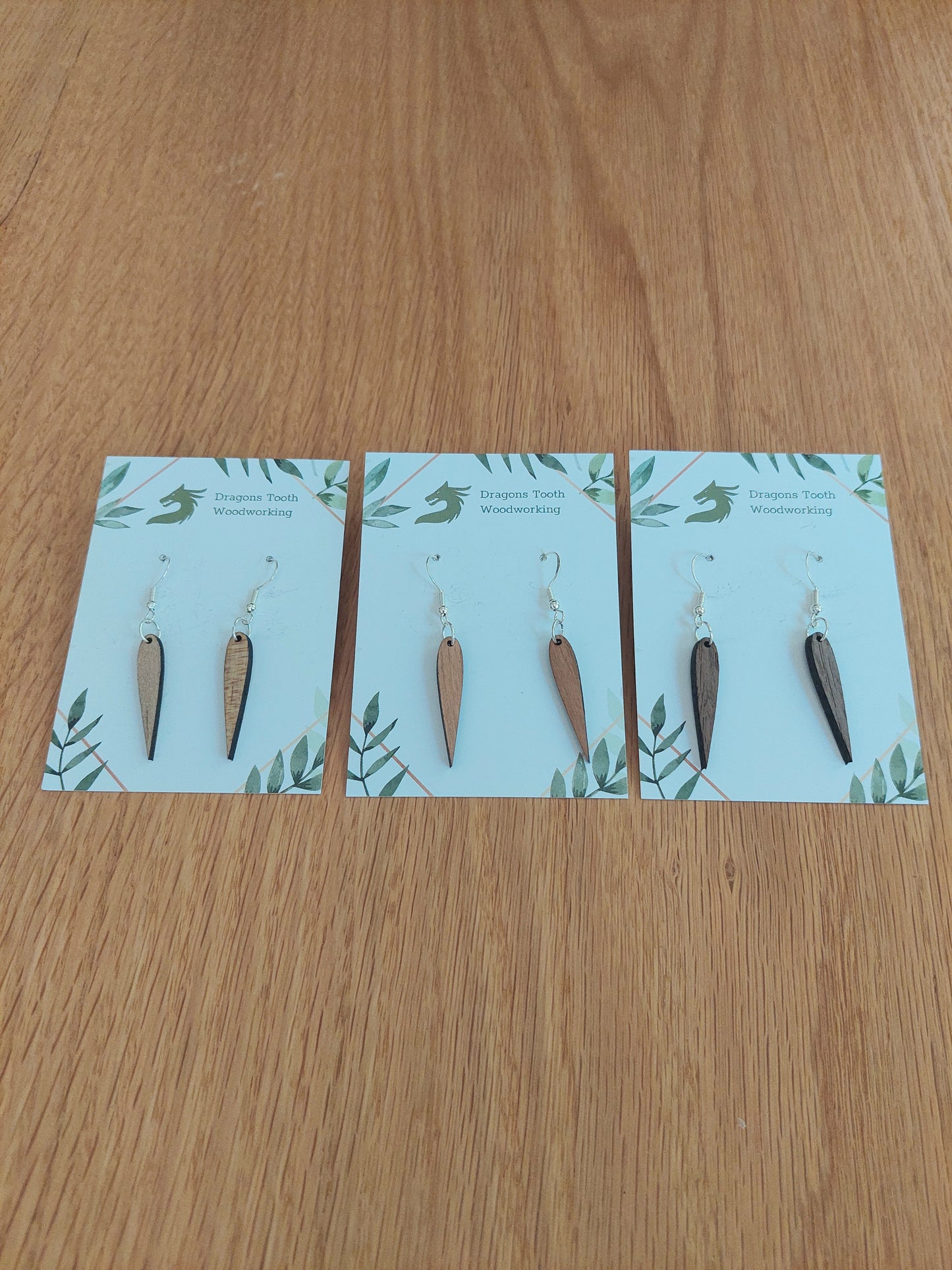 An alternate view displaying the pointed geometric dangle earrings in three available wood types: light Maple, warm Cherry, and deep Walnut.