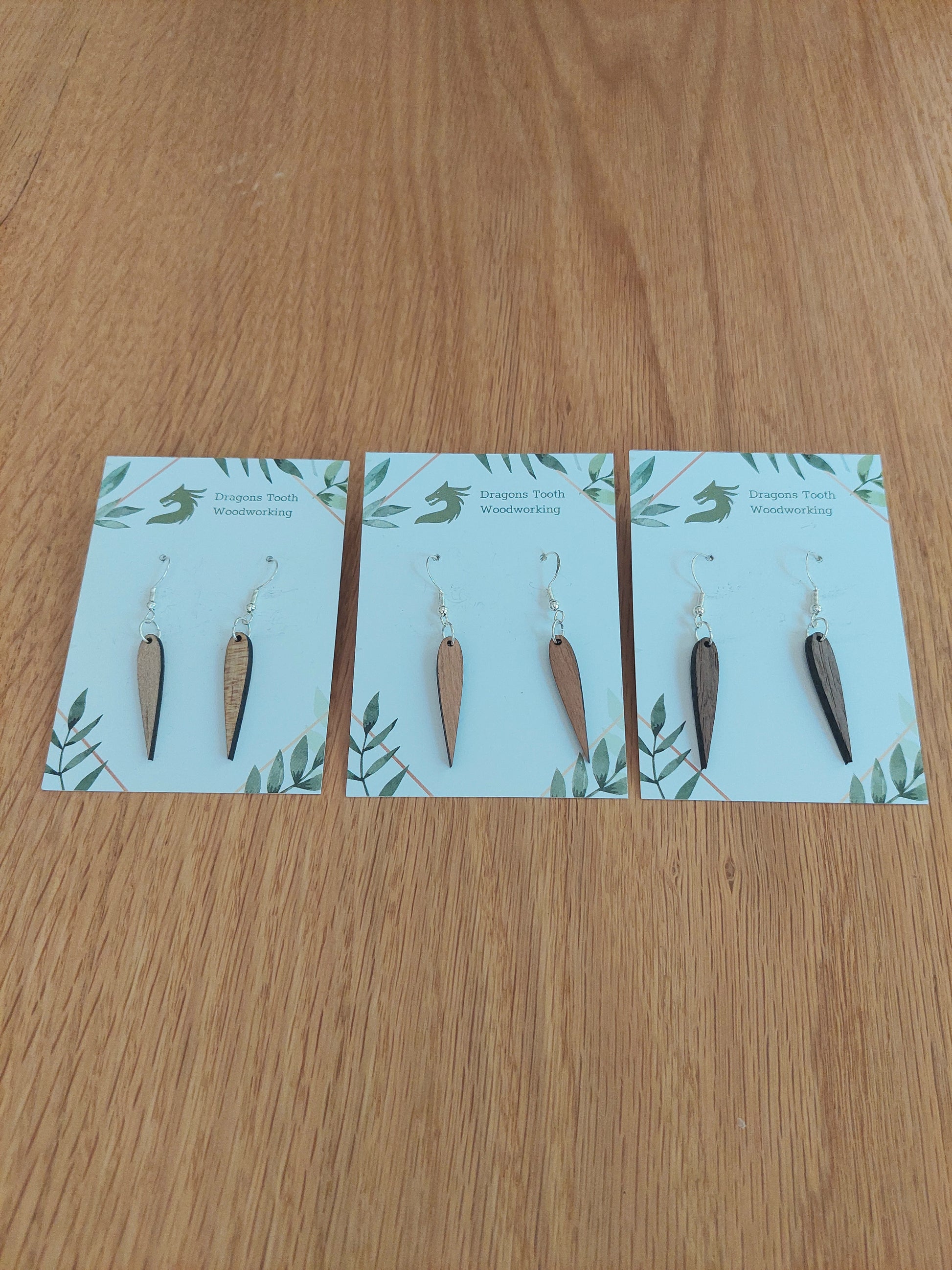 An alternate view displaying the pointed geometric dangle earrings in three available wood types: light Maple, warm Cherry, and deep Walnut.