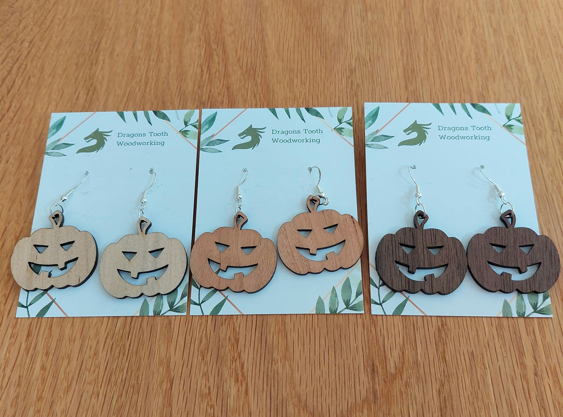 An alternate view displaying the jack-o'-lantern earrings in three available wood types: light Maple, warm Cherry, and deep Walnut.