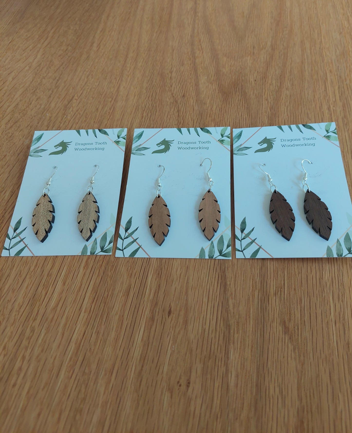 An alternate view displaying the simple leaf silhouette dangle earrings in three available wood types: light Maple, warm Cherry, and deep Walnut.