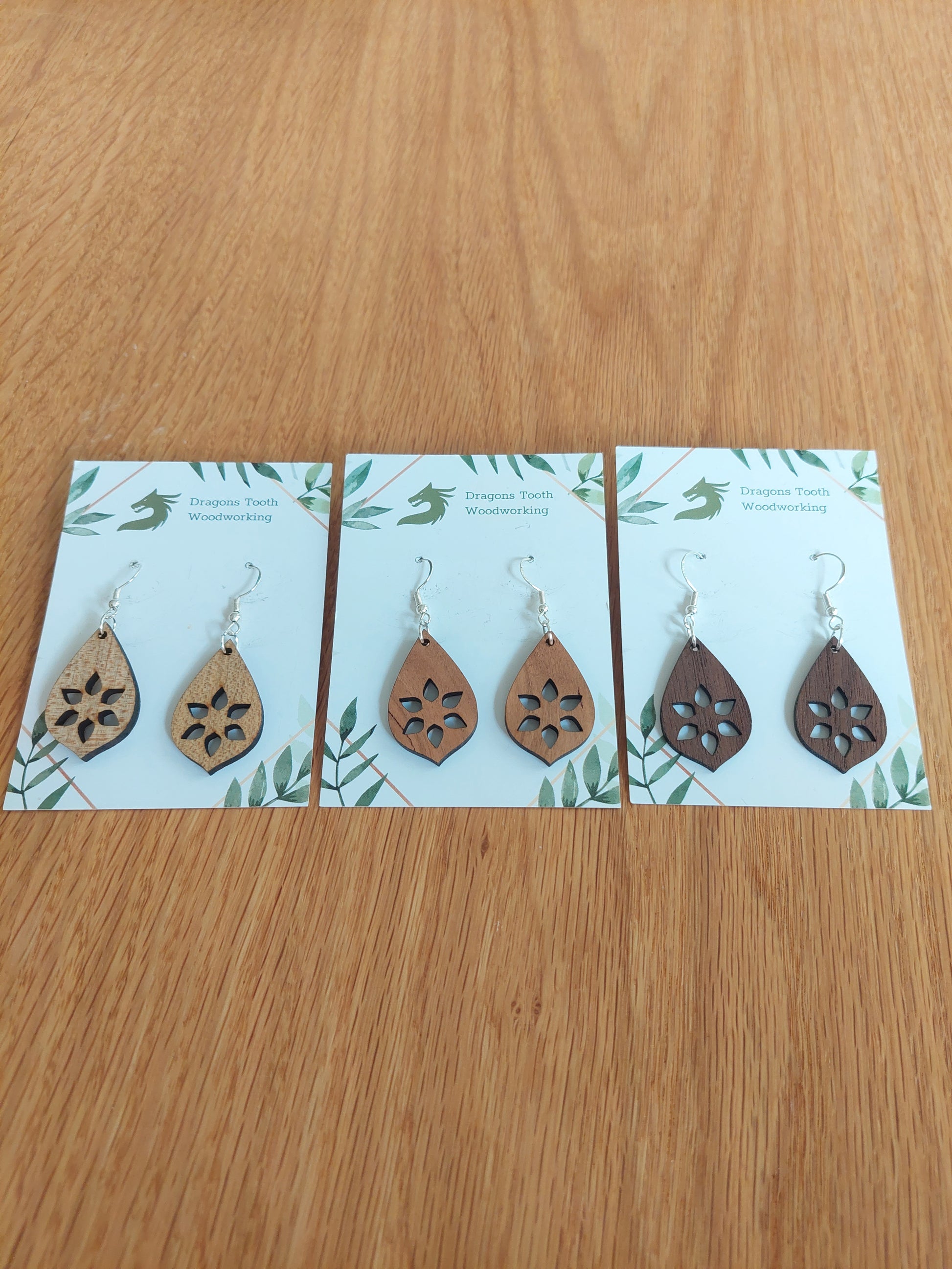 An alternate view displaying the star cutout dangle earrings in three available wood types: light Maple, warm Cherry, and deep Walnut.