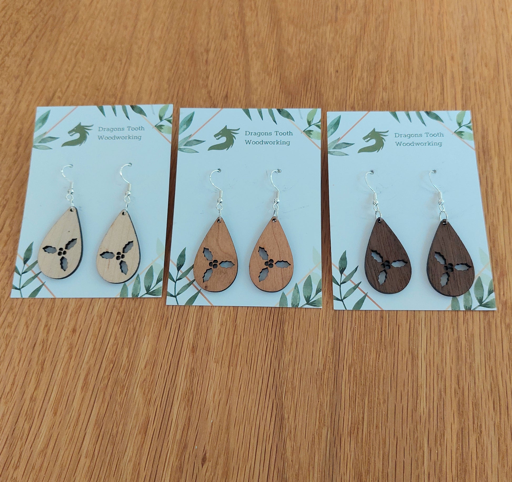An alternate view displaying the holly cluster teardrop earrings in three available wood types: light Maple, warm Cherry, and deep Walnut.