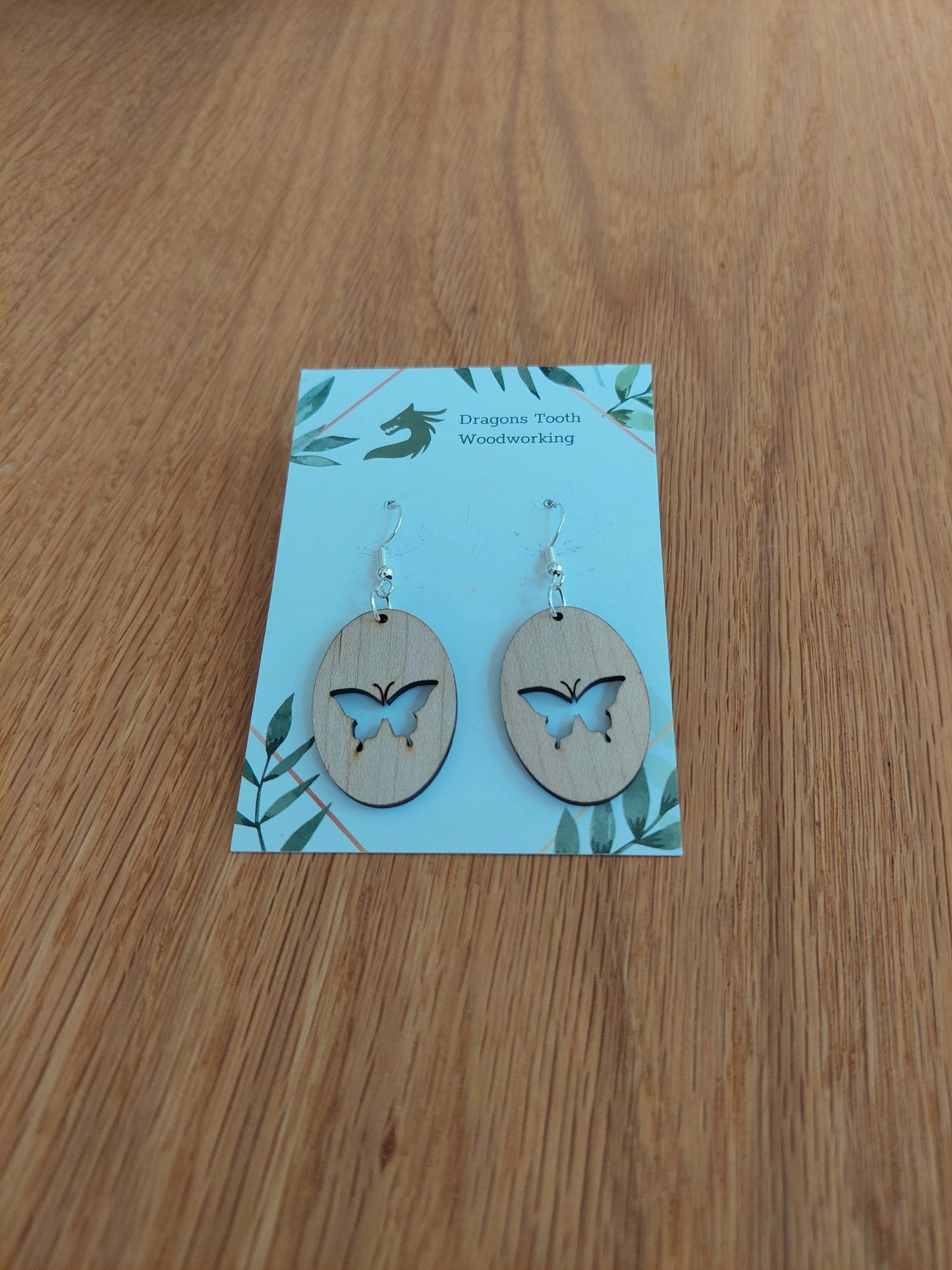 A front view of the butterfly earrings crafted from light, bright blonde solid Maple wood, displayed on an earring card.
