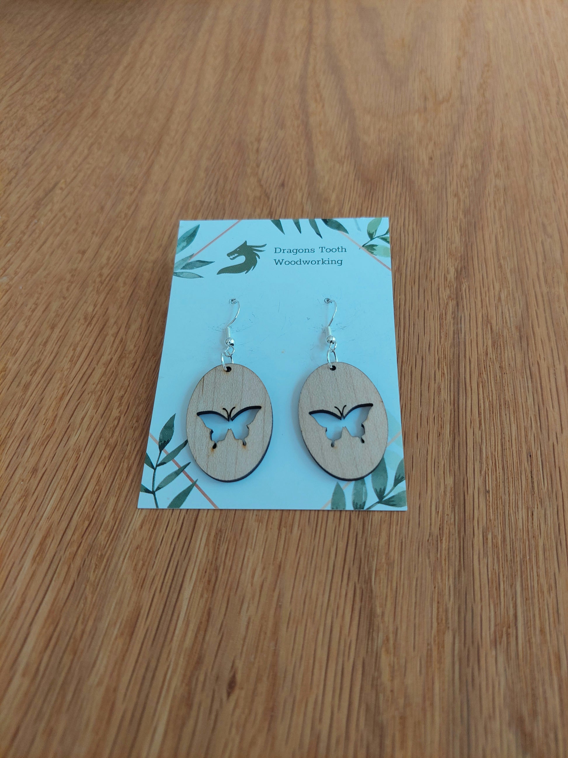 A front view of the butterfly earrings crafted from light, bright blonde solid Maple wood, displayed on an earring card.