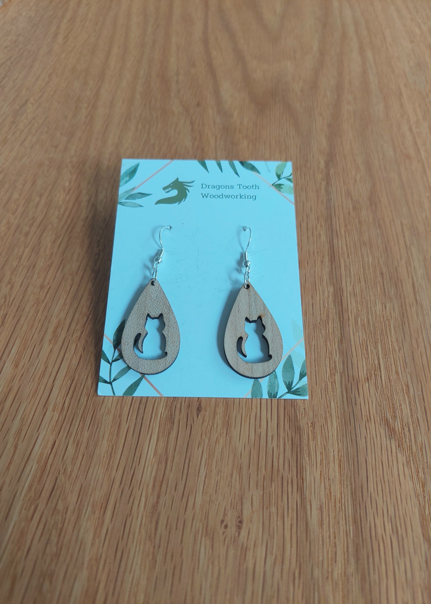 front view of the circular cat silhouette earrings crafted from light, bright blonde solid Maple wood, displayed on an earring card.