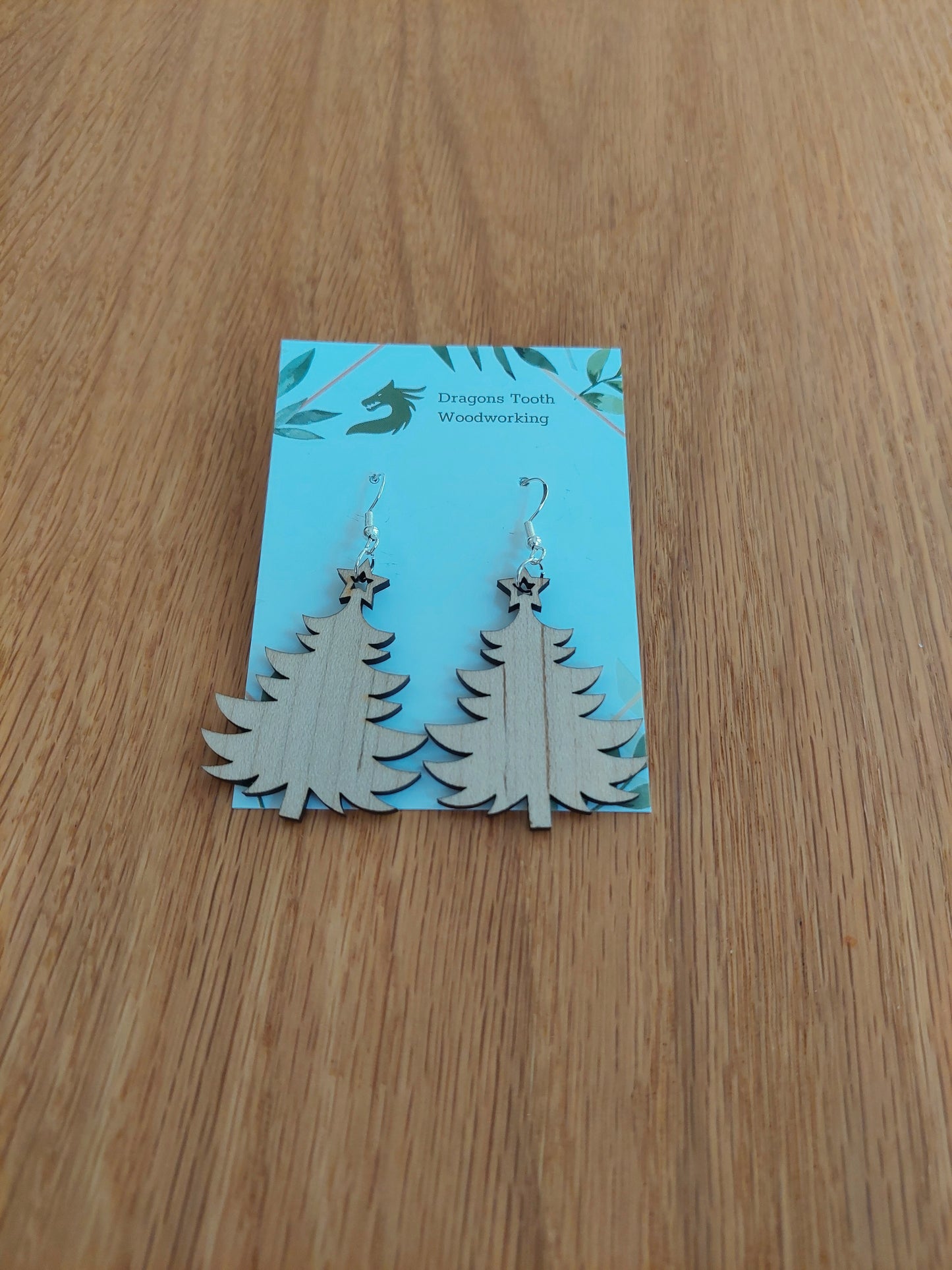 A front view of the Christmas tree earrings crafted from light, bright blonde solid Maple wood, displayed on an earring card.
