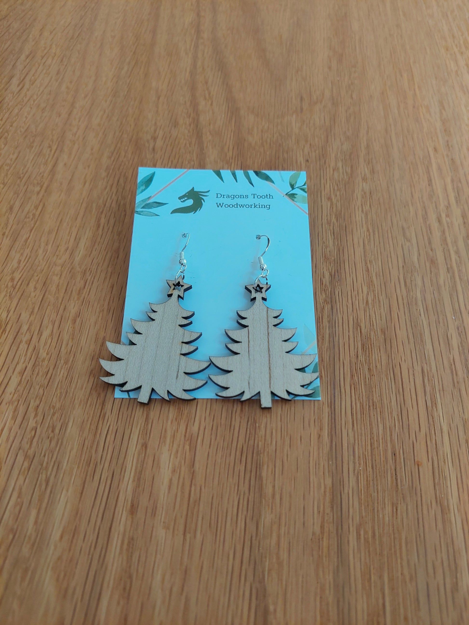 A front view of the Christmas tree earrings crafted from light, bright blonde solid Maple wood, displayed on an earring card.