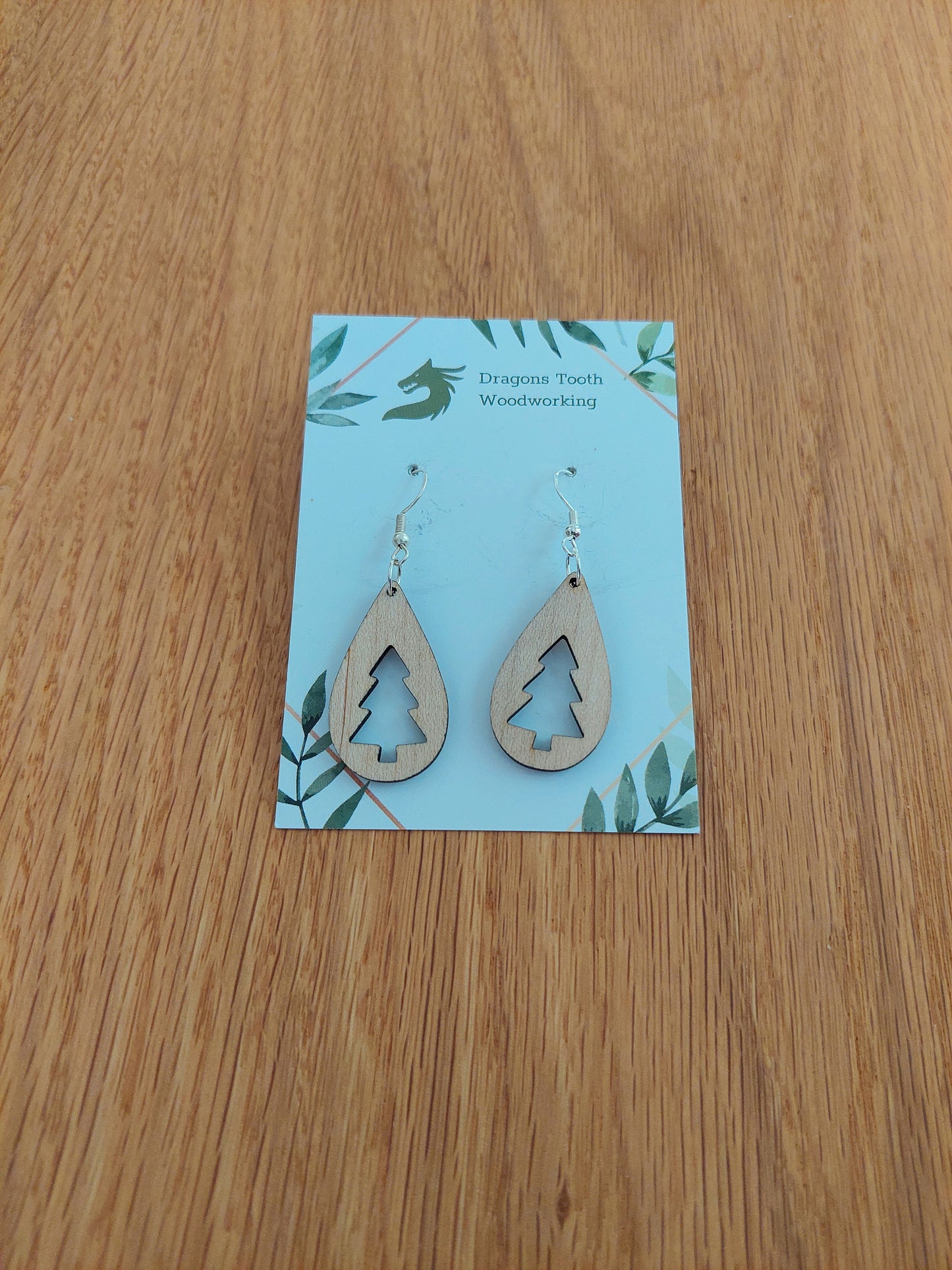 A front view of the Christmas tree teardrop earrings crafted from light, bright blonde solid Maple wood, displayed on an earring card.