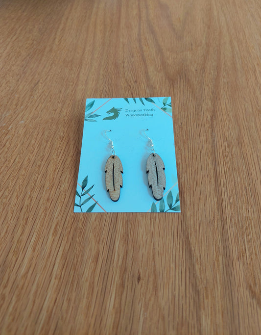 A front view of the intricate feather silhouette earrings crafted from light, bright blonde solid Maple wood, displayed on an earring card.
