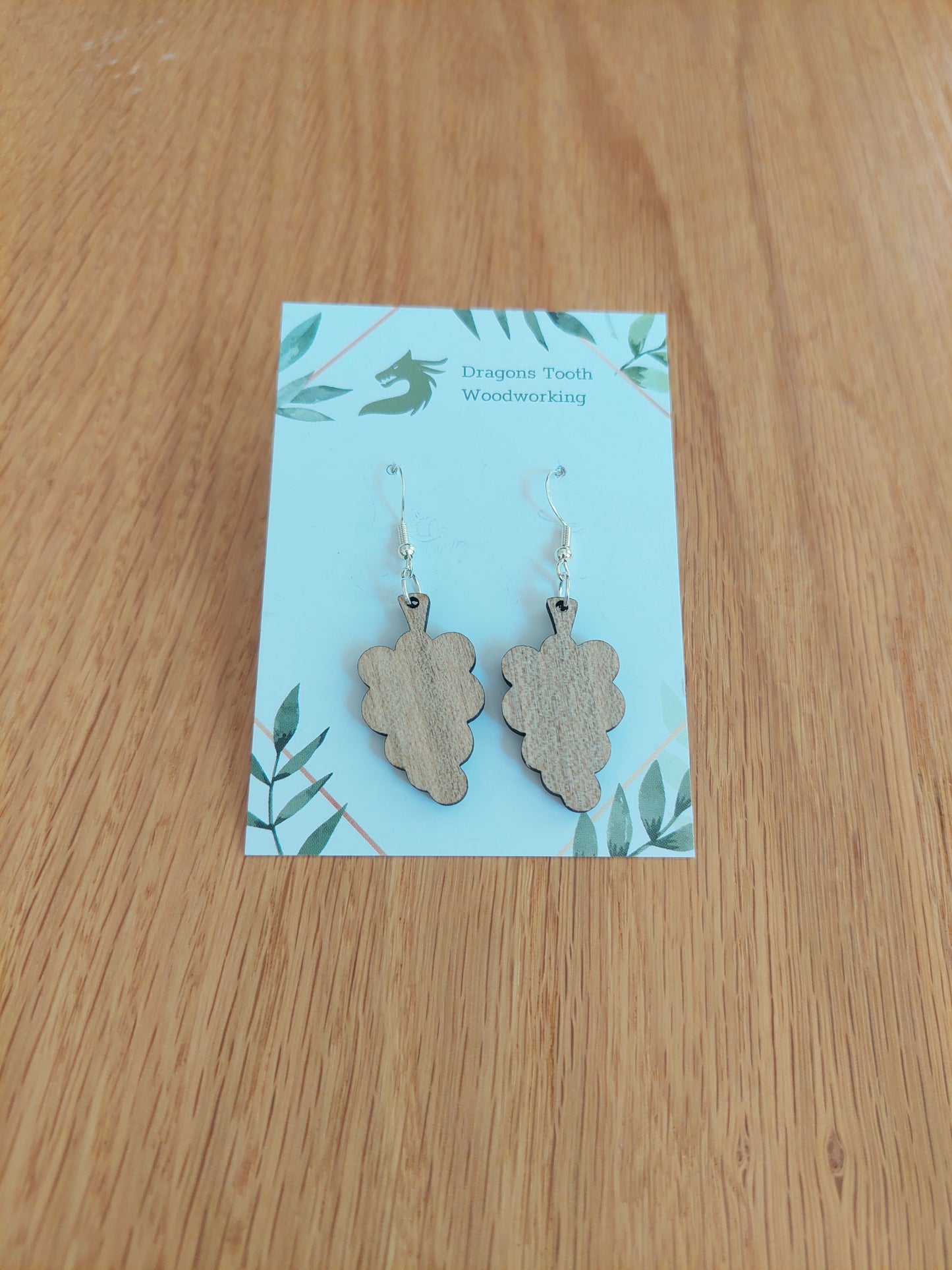 A front view of the grape cluster earrings crafted from light, bright blonde solid Maple wood, displayed on an earring card.