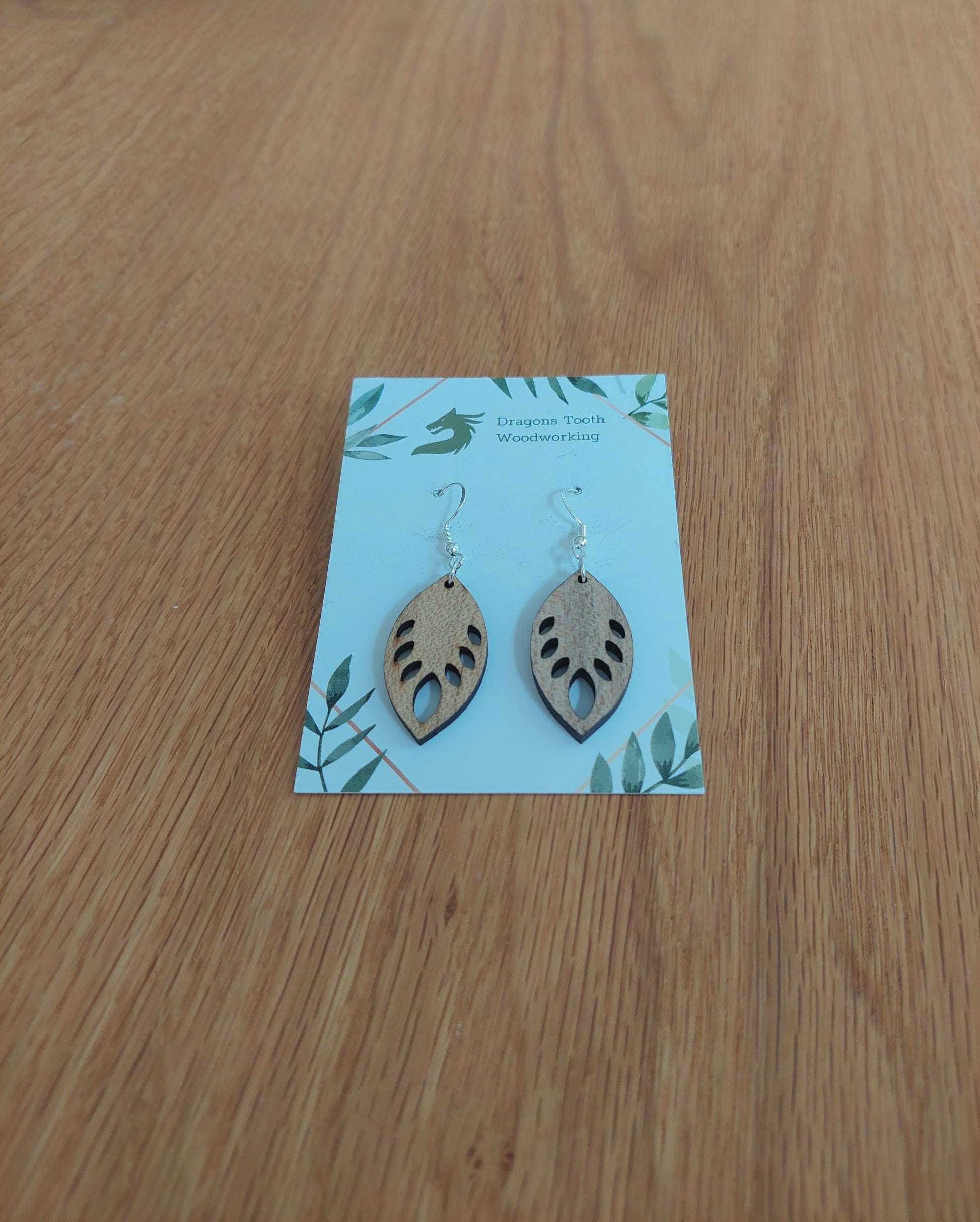 A front view of the monstera leaf earrings crafted from light, bright blonde solid Maple wood, displayed on an earring card.