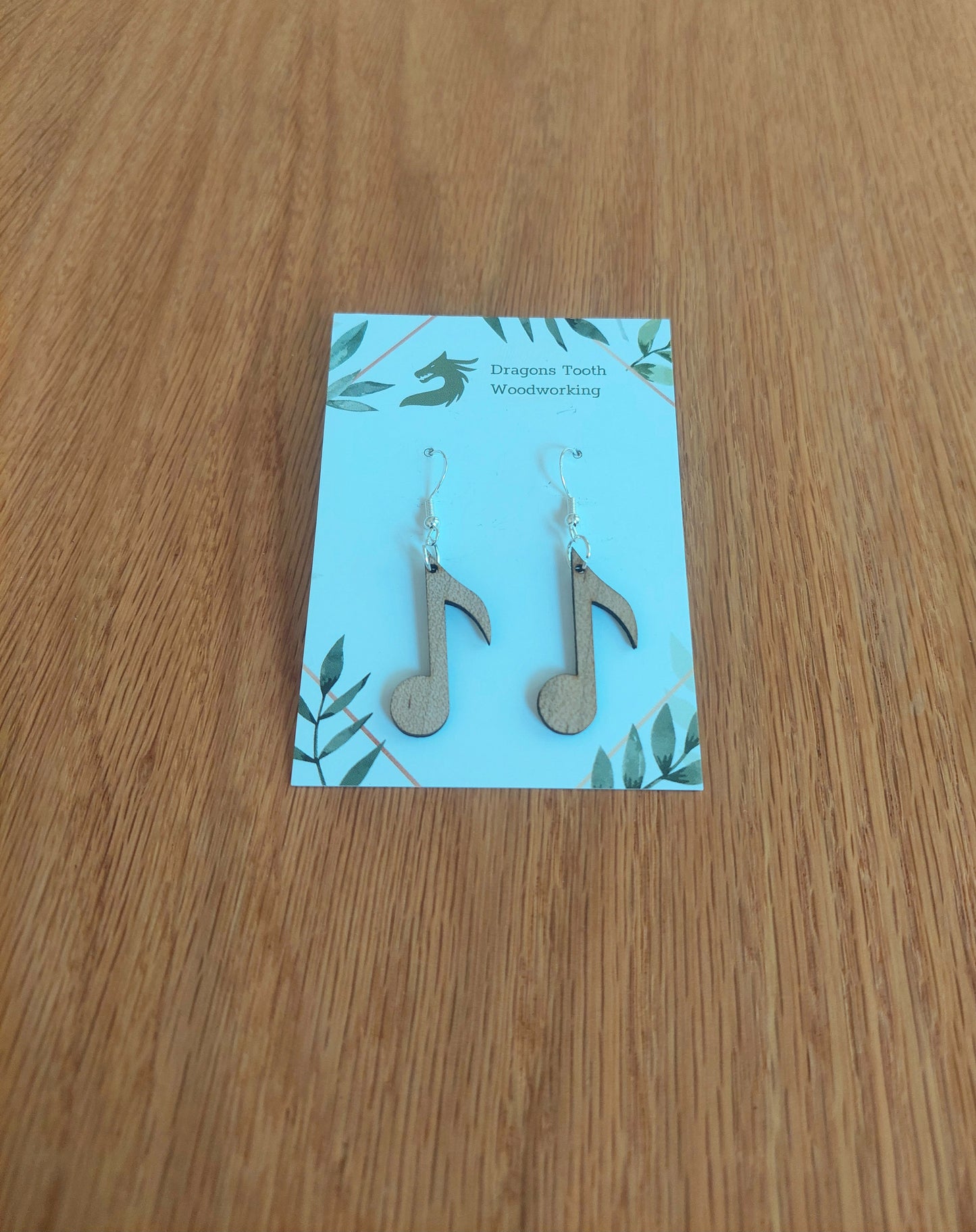 A front view of the circular music note earrings crafted from light, bright blonde solid Maple wood, displayed on an earring card.