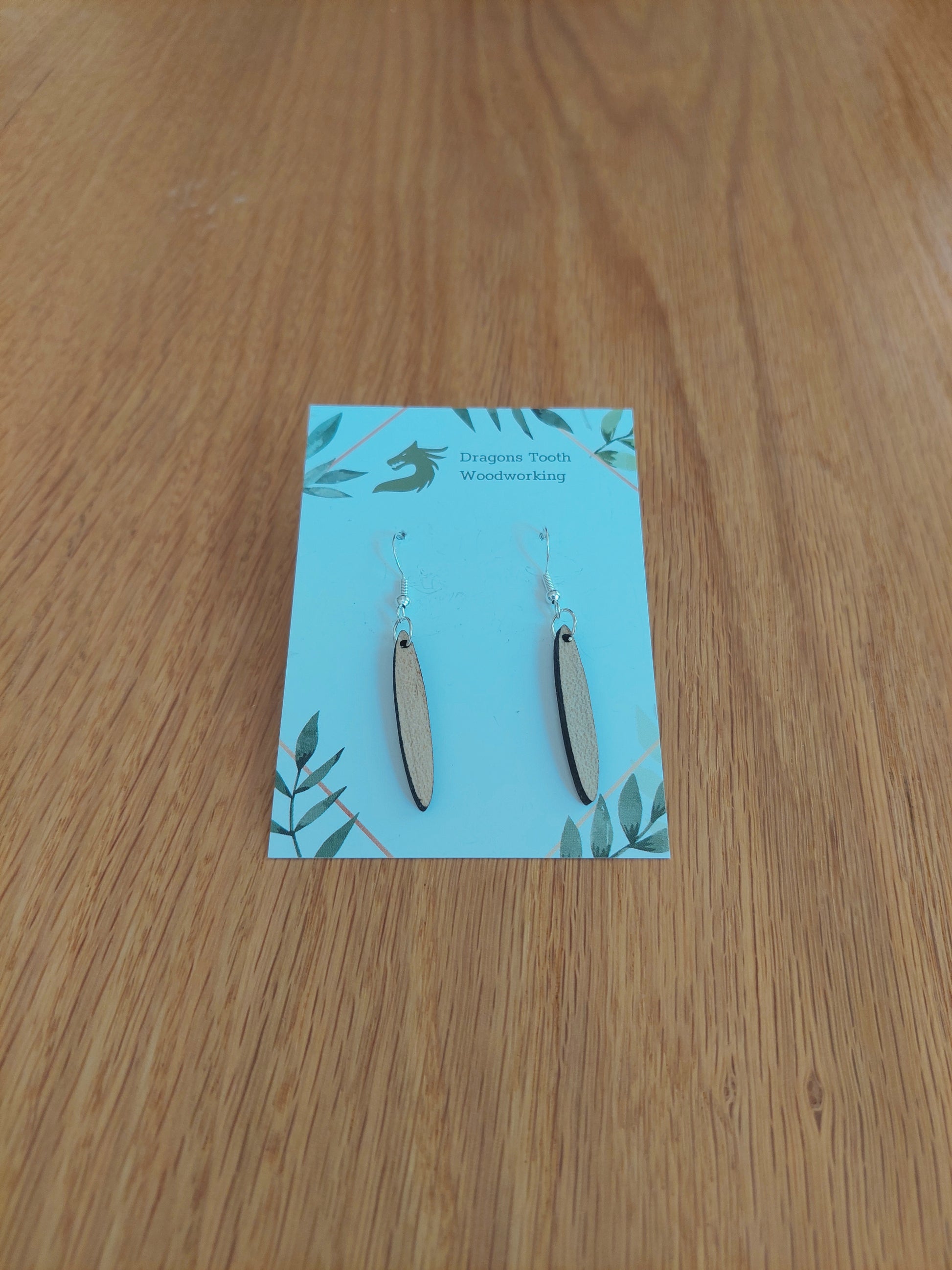 A front view of the minimalist open oval earrings crafted from light, bright blonde solid Maple wood, displayed on an earring card.