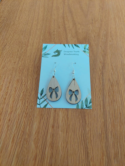 A front view of the ribbon bow teardrop earrings crafted from light, bright blonde solid Maple wood, displayed on an earring card.