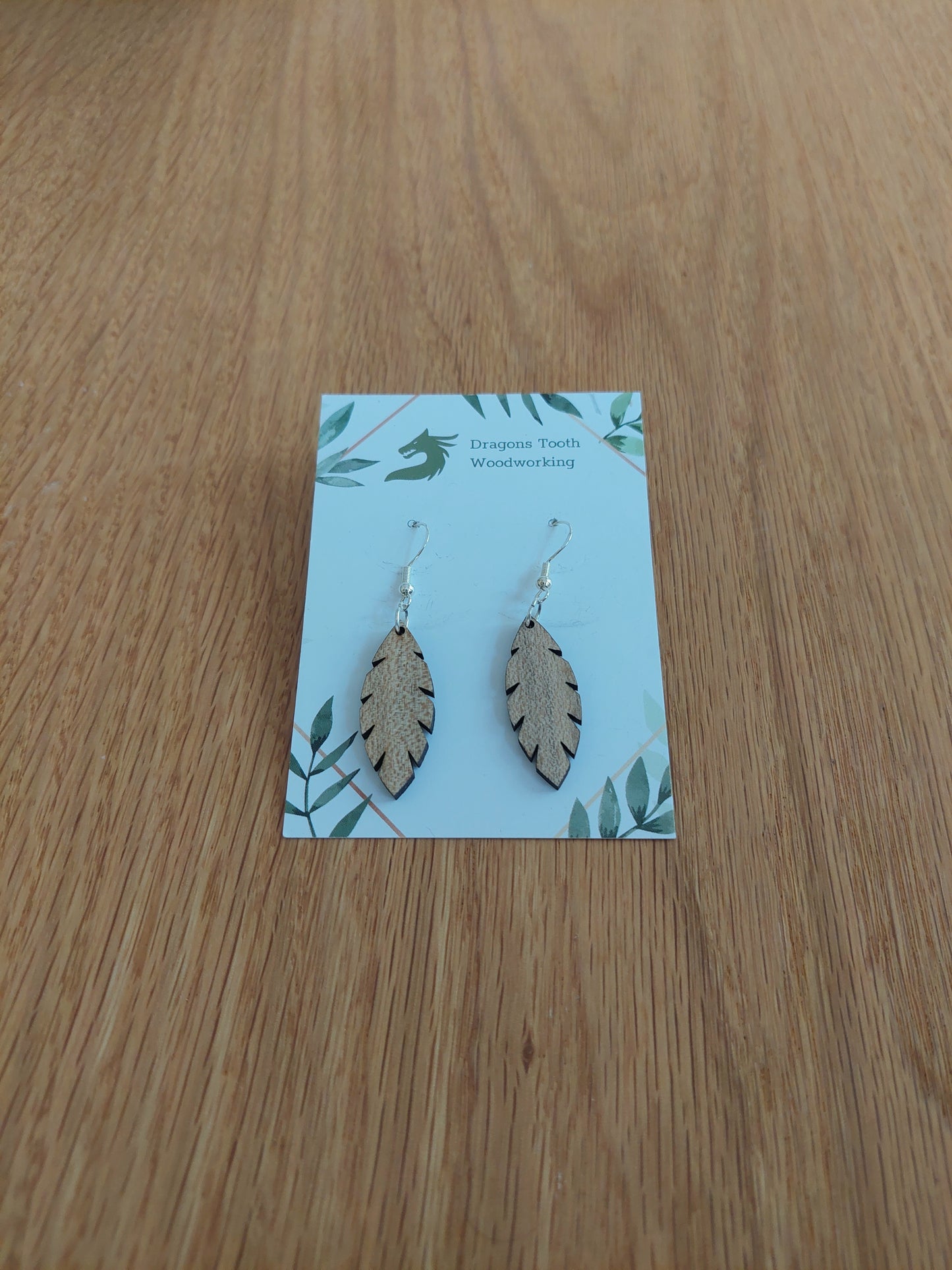 A front view of the minimalist simple leaf earrings crafted from light, bright blonde solid Maple wood, displayed on an earring card.
