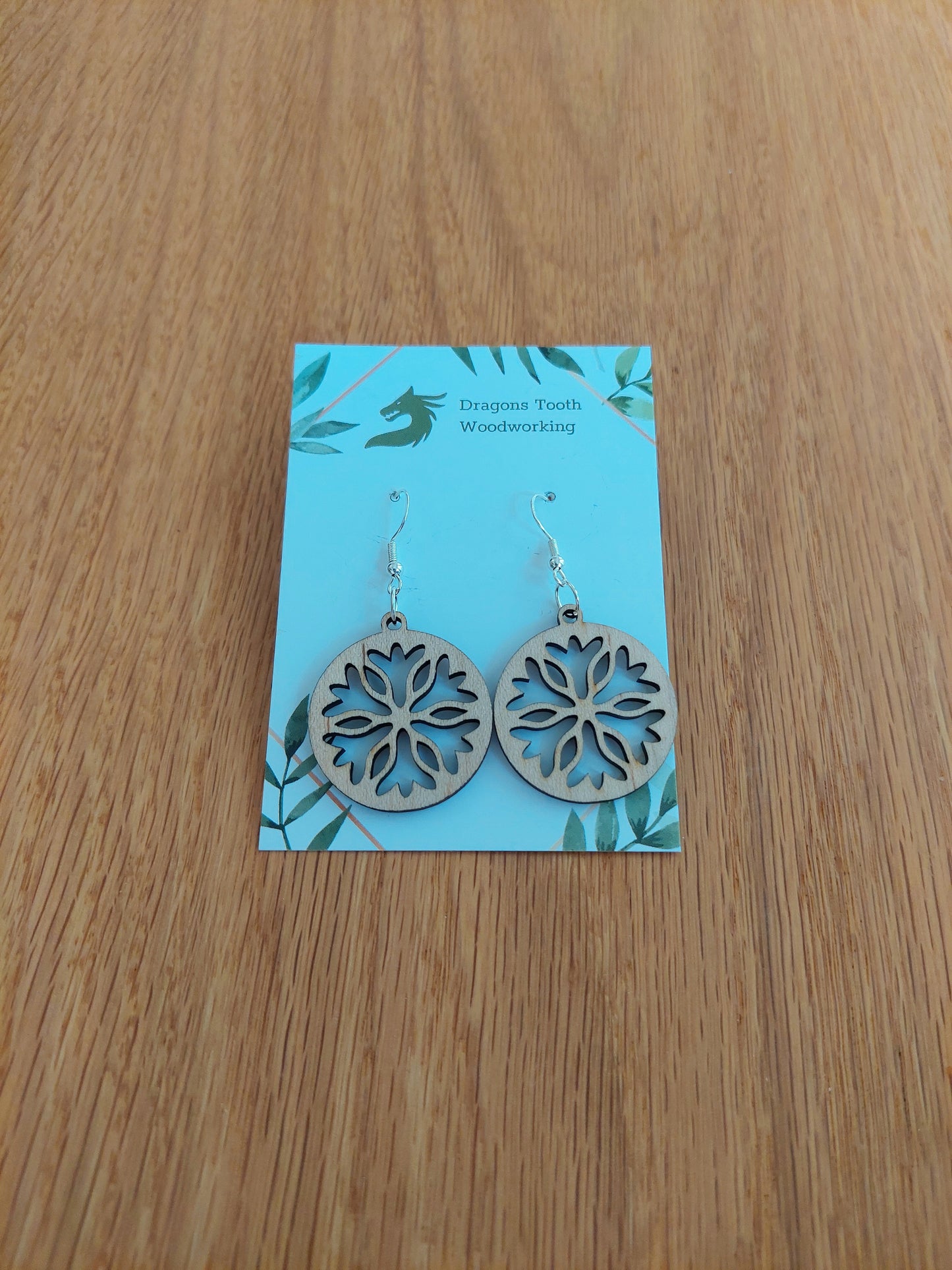 A front view of the classic snowflake silhouette earrings crafted from light, bright blonde solid Maple wood, displayed on an earring card.