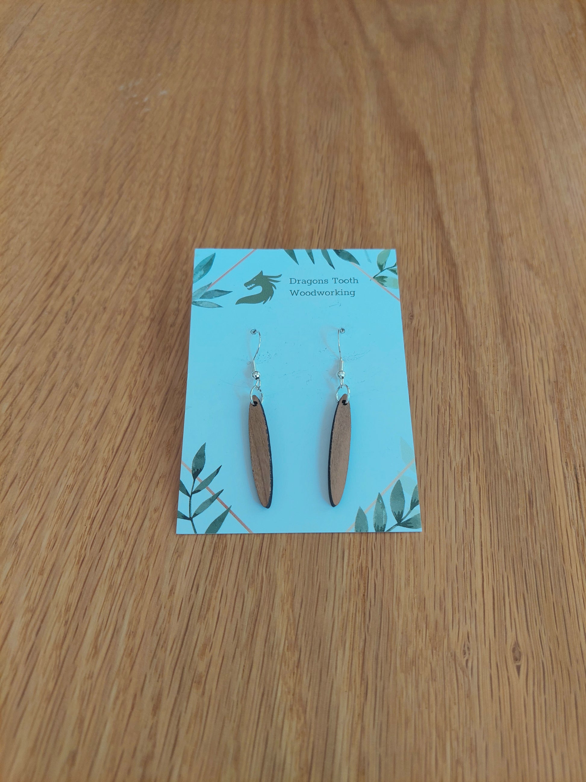 Front view of a pair of cherry wood minimalist open oval dangle earrings displayed on a rustic earring card.