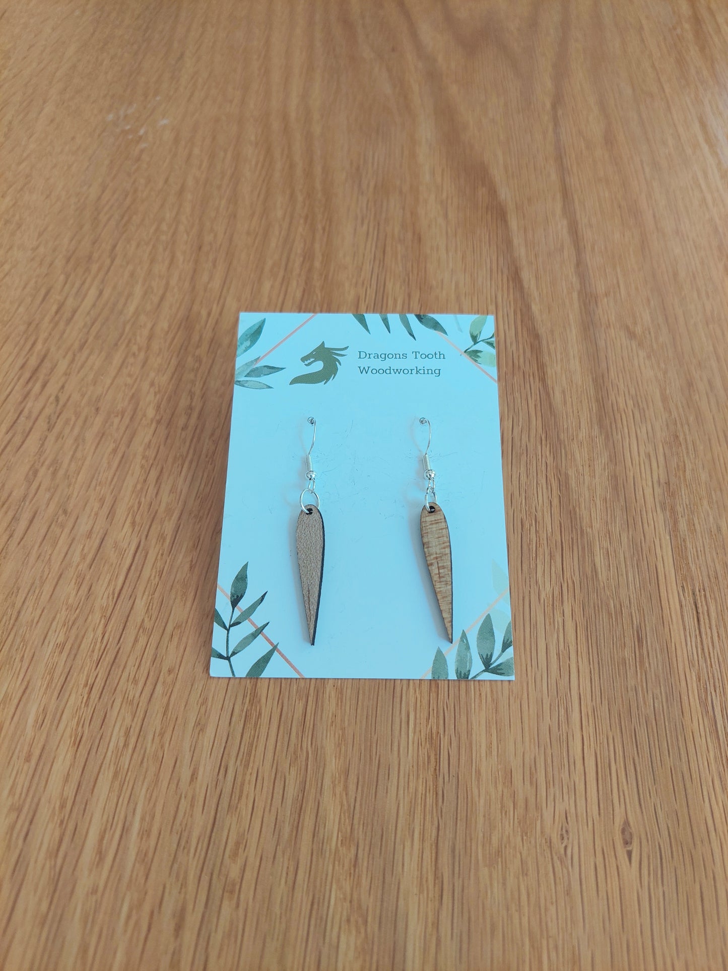 Front view of a pair of maple wood minimalist pointed geometric dangle earrings displayed on a rustic earring card.