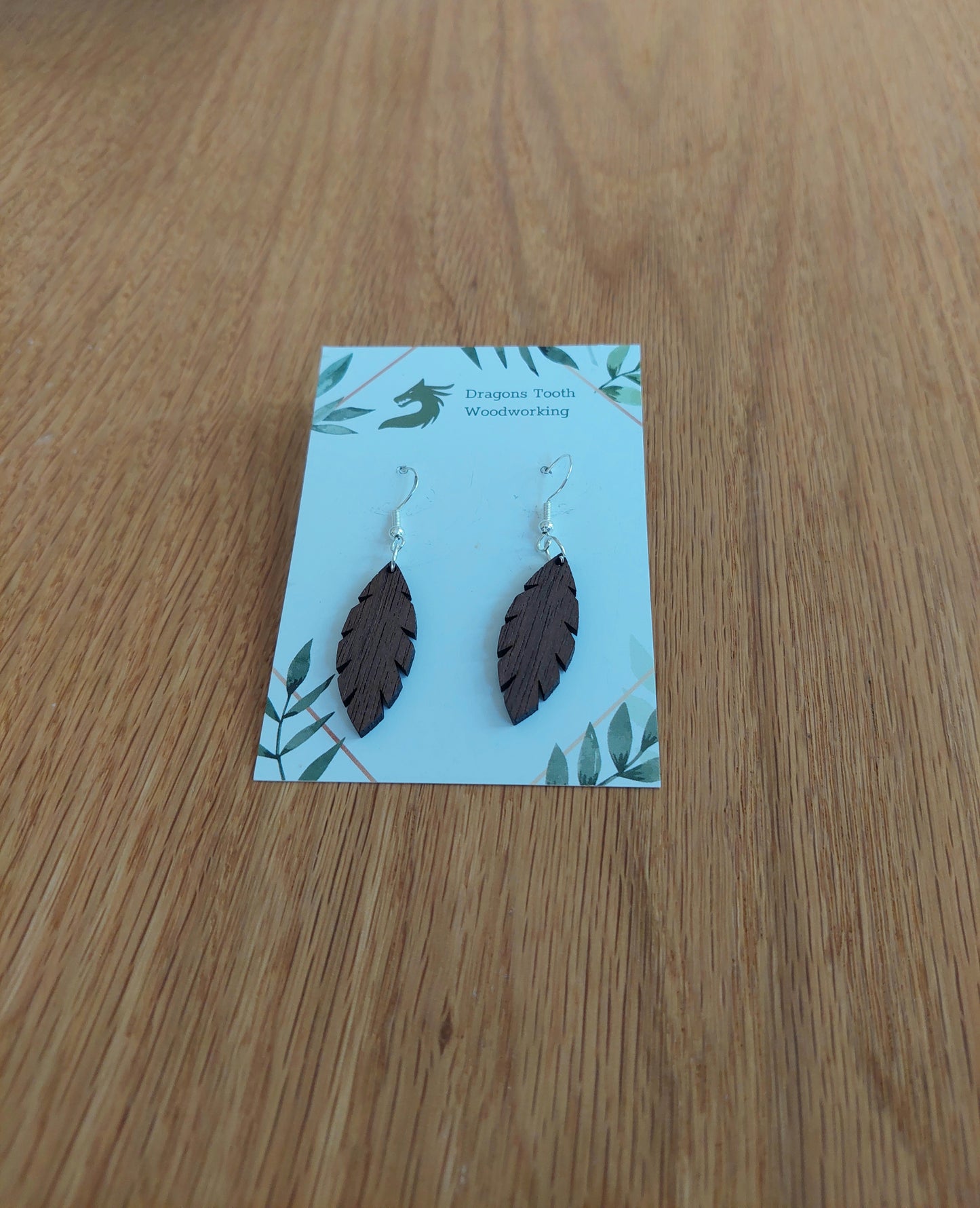 Front view of a pair of walnut wood minimalist simple leaf silhouette dangle earrings displayed on a rustic earring card.