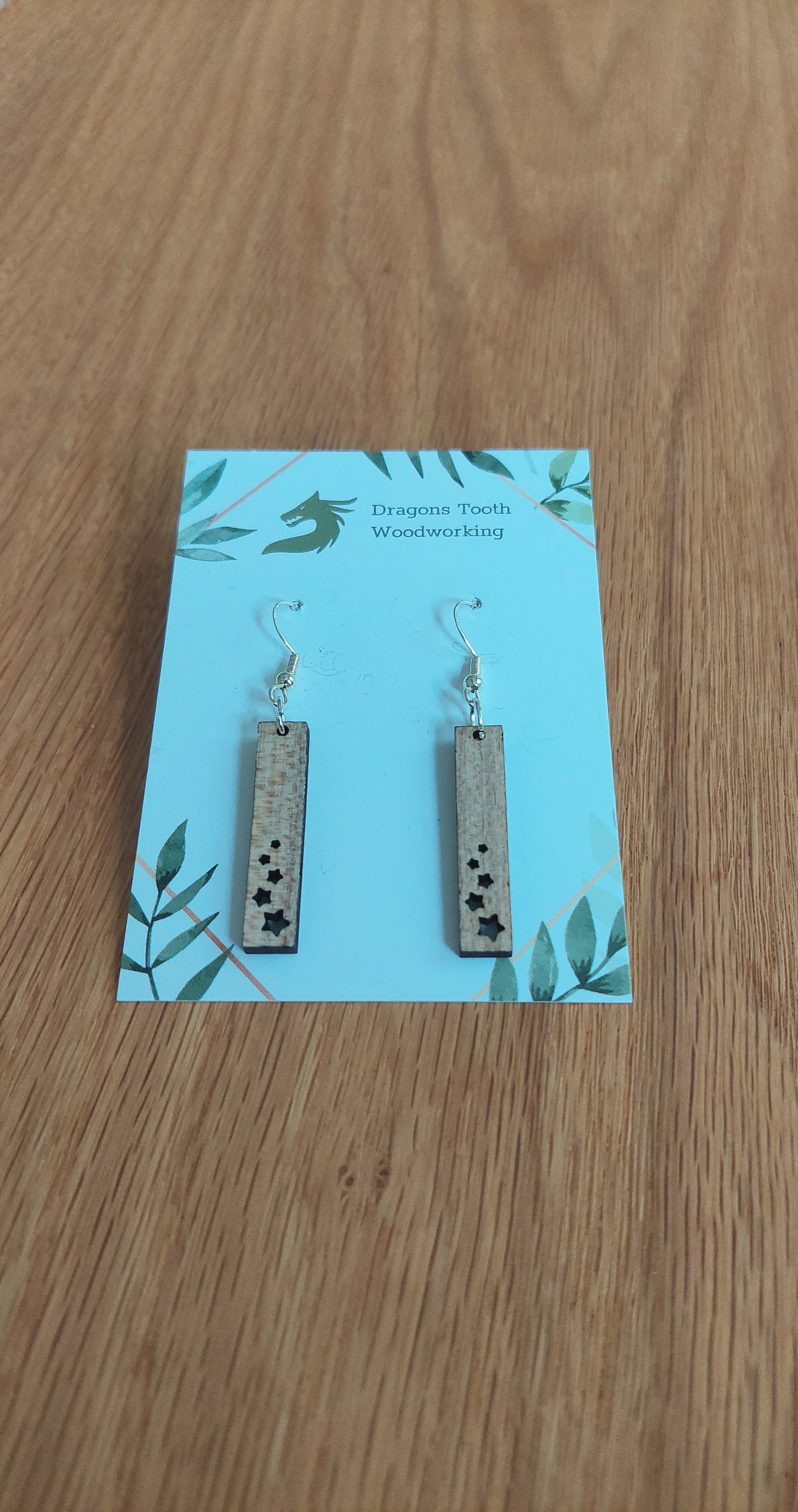 Front view of a pair of maple wood minimalist star shower geometric dangle earrings displayed on a rustic earring card.