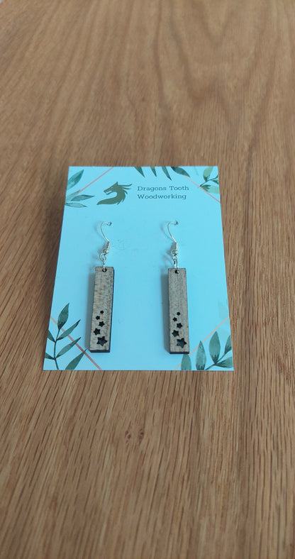 Front view of a pair of maple wood minimalist star shower geometric dangle earrings displayed on a rustic earring card.