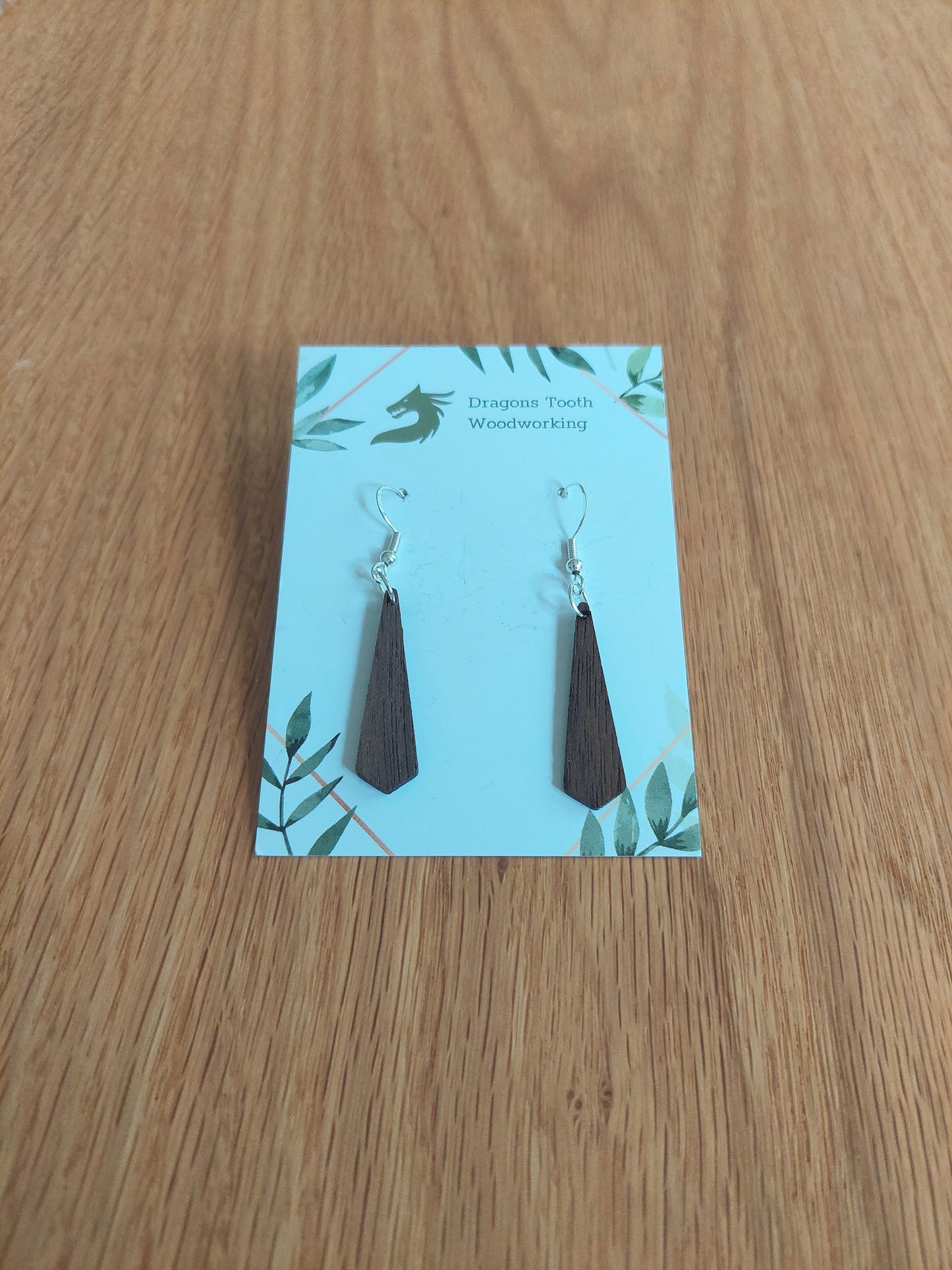 Front view of a pair of walnut wood minimalist tie silhouette geometric dangle earrings displayed on a rustic earring card.