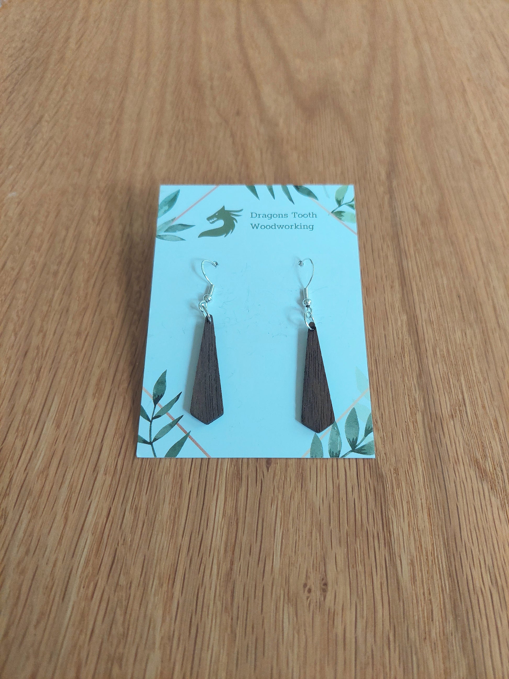 Front view of a pair of walnut wood minimalist tie silhouette geometric dangle earrings displayed on a rustic earring card.