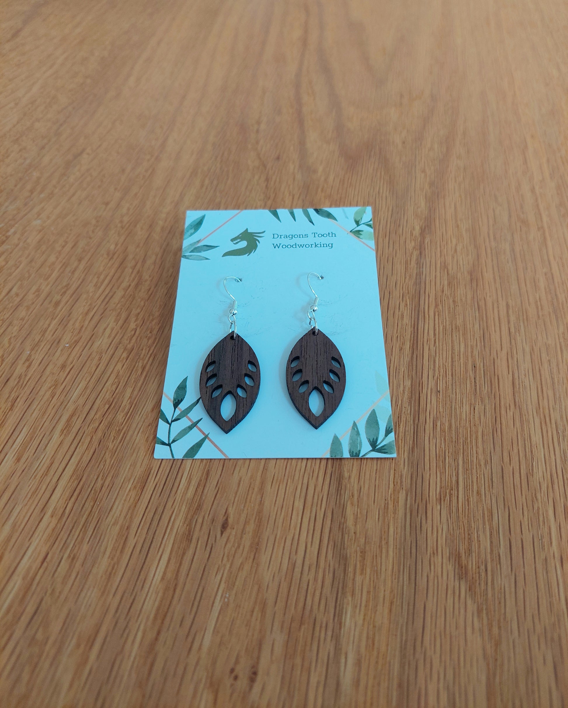 Front view of a pair of walnut wood monstera leaf dangle earrings displayed on a rustic earring card