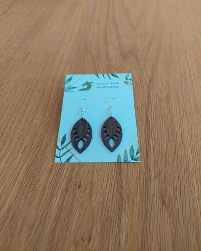 Front view of a pair of walnut wood monstera leaf dangle earrings displayed on a rustic earring card