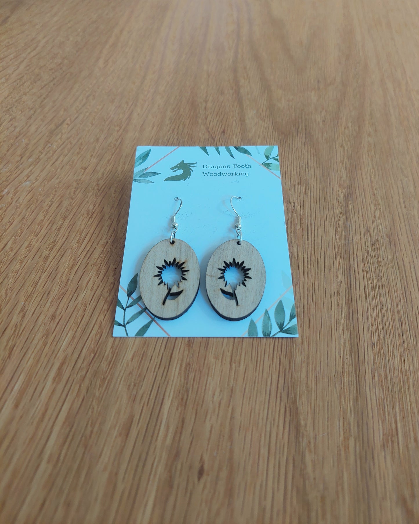 A front view of the aster flower earrings crafted from light, bright blonde solid Maple wood, displayed on an earring card