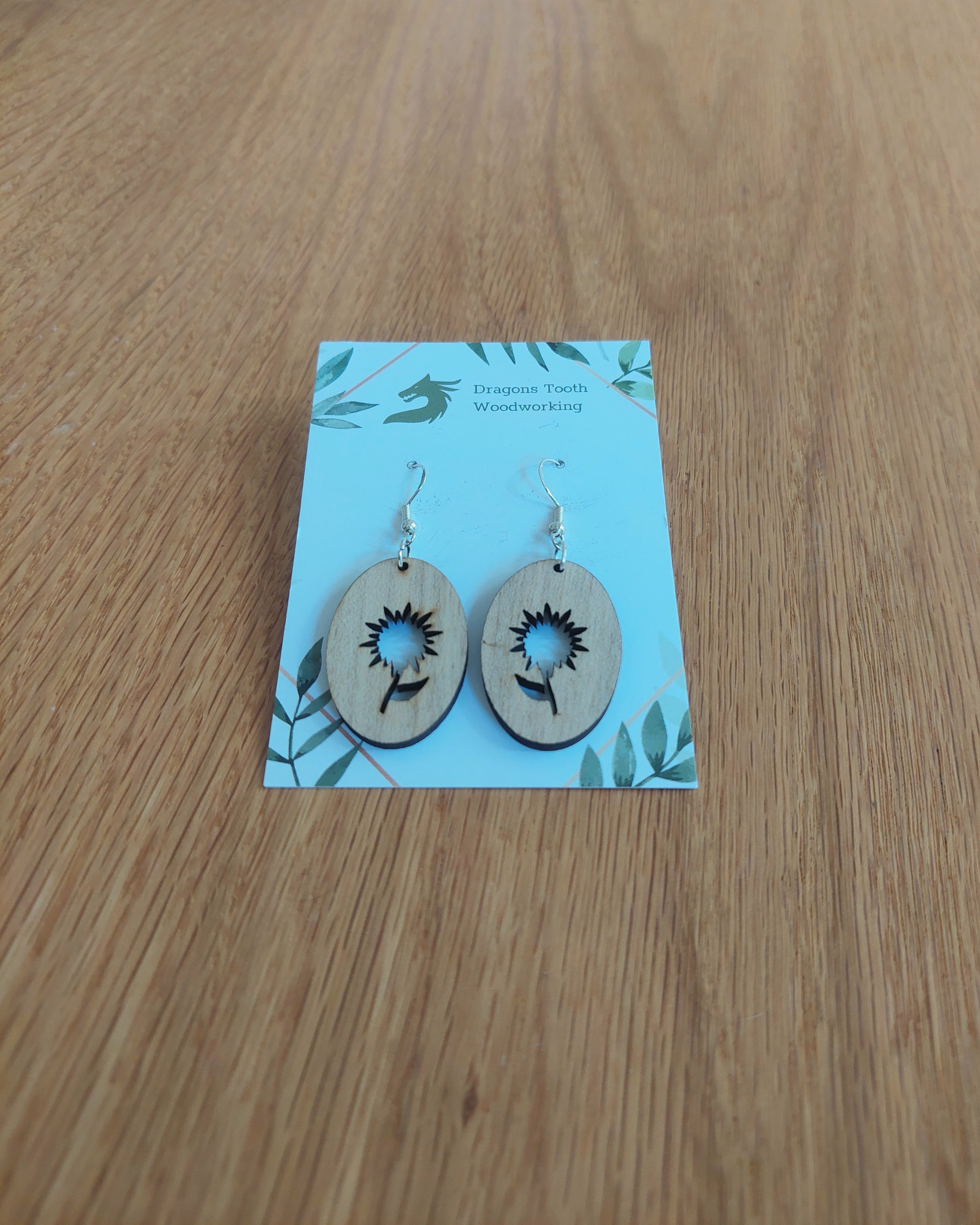A front view of the aster flower earrings crafted from light, bright blonde solid Maple wood, displayed on an earring card