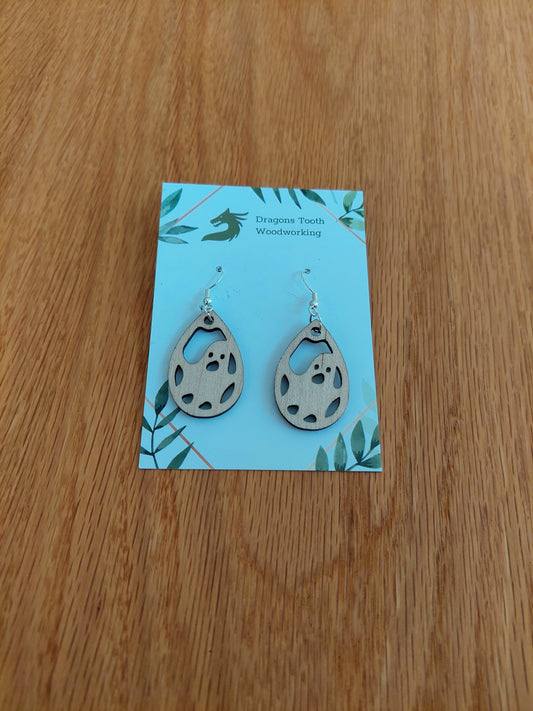 Front view of a pair of maple wood friendly ghost dangle earrings displayed on a rustic earring card.