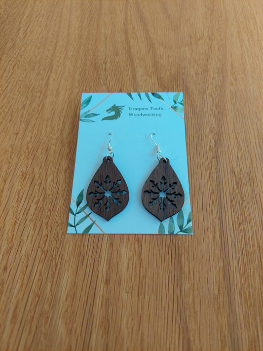 A front view of the large snowflake teardrop earrings crafted from rich, deep chocolate-brown solid Walnut wood, displayed on an earring card.